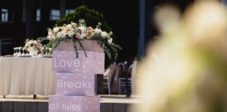 Plenerowa aranżacja ślubu z kwiatami i napisem Love Breaks all rules