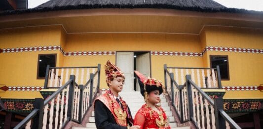Tradycje ślubne na Podhalu, Śląsku i Kaszubach – inspiracje na regionalne akcenty w waszym przyjęciu weselnym Para młoda w tradycyjnych strojach Batak przed domem w Sumatrze